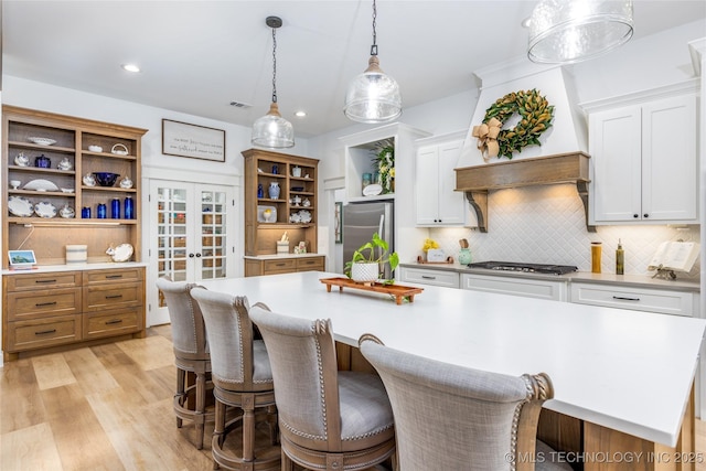 kitchen with light wood finished floors, stainless steel appliances, white cabinetry, open shelves, and light countertops