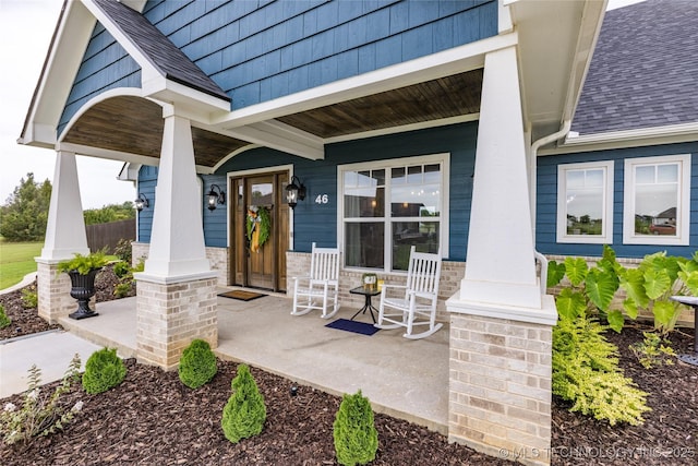 doorway to property with a porch and a shingled roof
