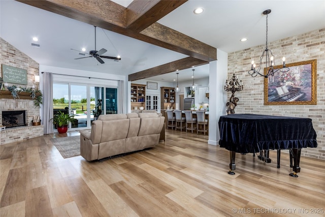 living room with light wood-style flooring, a brick fireplace, brick wall, and ceiling fan with notable chandelier