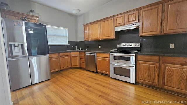 506 S Delaware Ave, Okmulgee, OK 74447 - kitchen with stainless steel appliances, a sink, dark countertops, brown cabinets, and under cabinet range hood