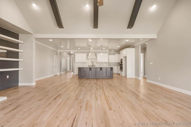 unfurnished living room with vaulted ceiling with beams, baseboards, a sink, and light wood-style floors