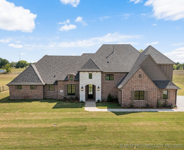 french provincial home with stone siding, board and batten siding, a shingled roof, a front yard, and brick siding