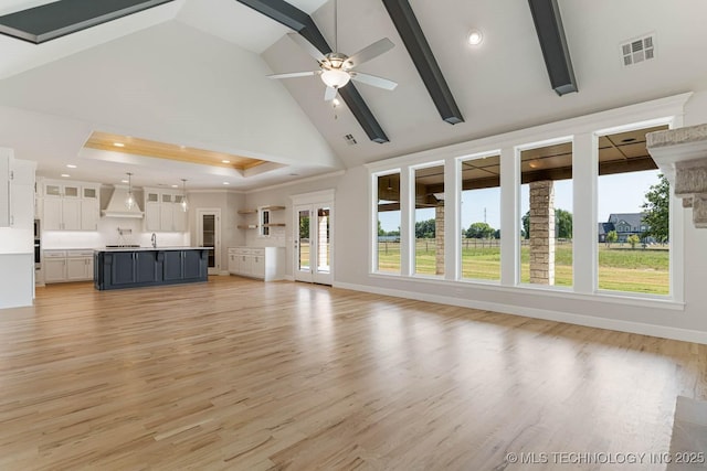 unfurnished living room with high vaulted ceiling, a ceiling fan, light wood-type flooring, a tray ceiling, and visible vents