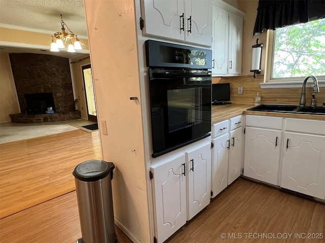 1380 N Lakeview Ave, Mannford, OK 74044 - kitchen featuring wood finished floors, oven, a stone fireplace, white cabinetry, and a sink