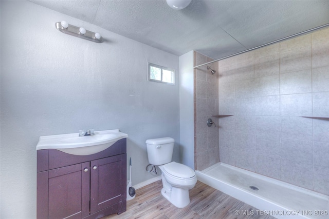 bathroom with a textured ceiling, tiled shower, toilet, wood finished floors, and vanity