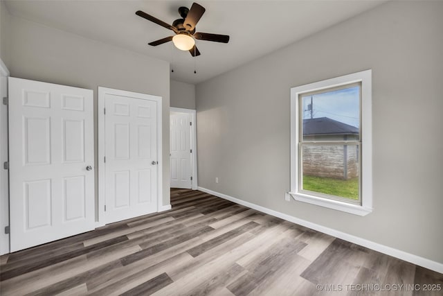 unfurnished bedroom with baseboards, wood finished floors, ceiling fan, and multiple windows