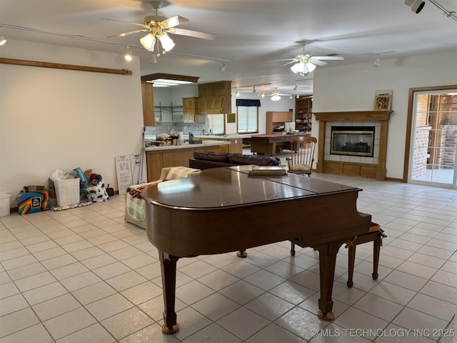 recreation room with track lighting, a tile fireplace, a ceiling fan, and light tile patterned floors