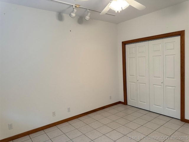 unfurnished bedroom featuring track lighting, ceiling fan, baseboards, and light tile patterned floors