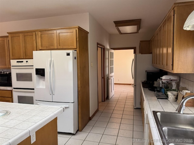 kitchen with brown cabinets, tile countertops, light tile patterned floors, a sink, and white appliances