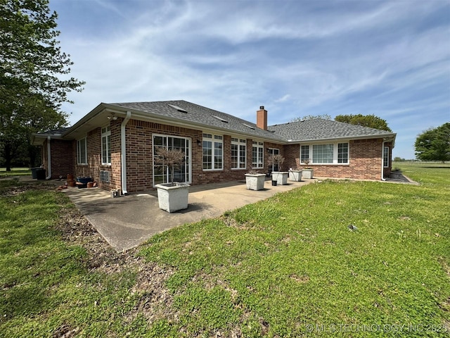back of house with a chimney, a shingled roof, a patio area, a lawn, and brick siding