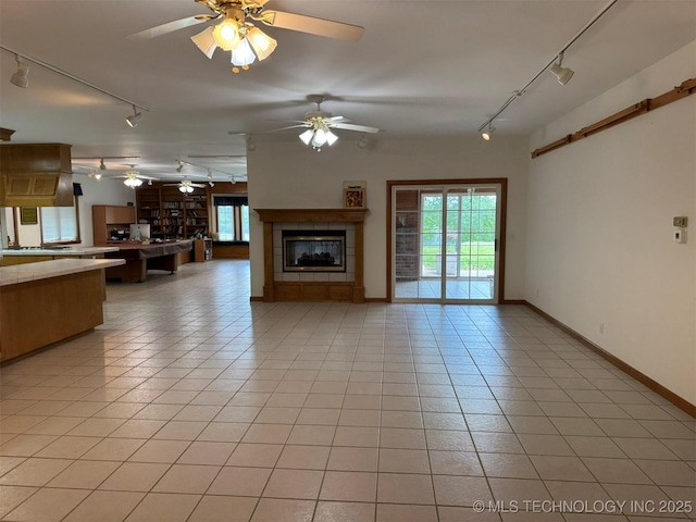 402325 W 2100th Rd, Bartlesville, OK 74006 - unfurnished living room featuring track lighting, a tile fireplace, ceiling fan, light tile patterned flooring, and baseboards