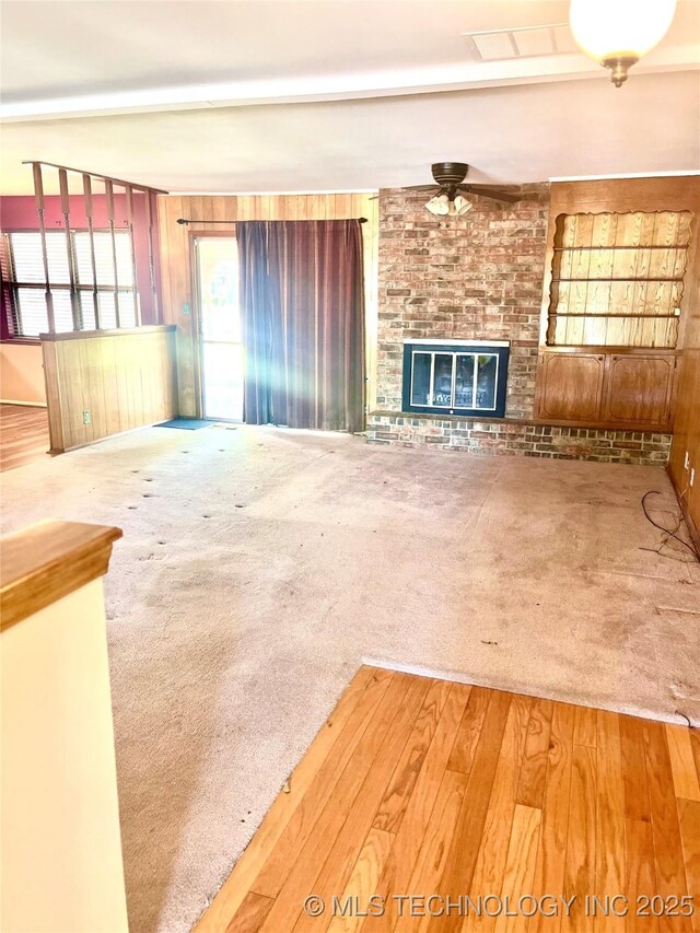 unfurnished living room featuring ceiling fan, a brick fireplace, and carpet flooring