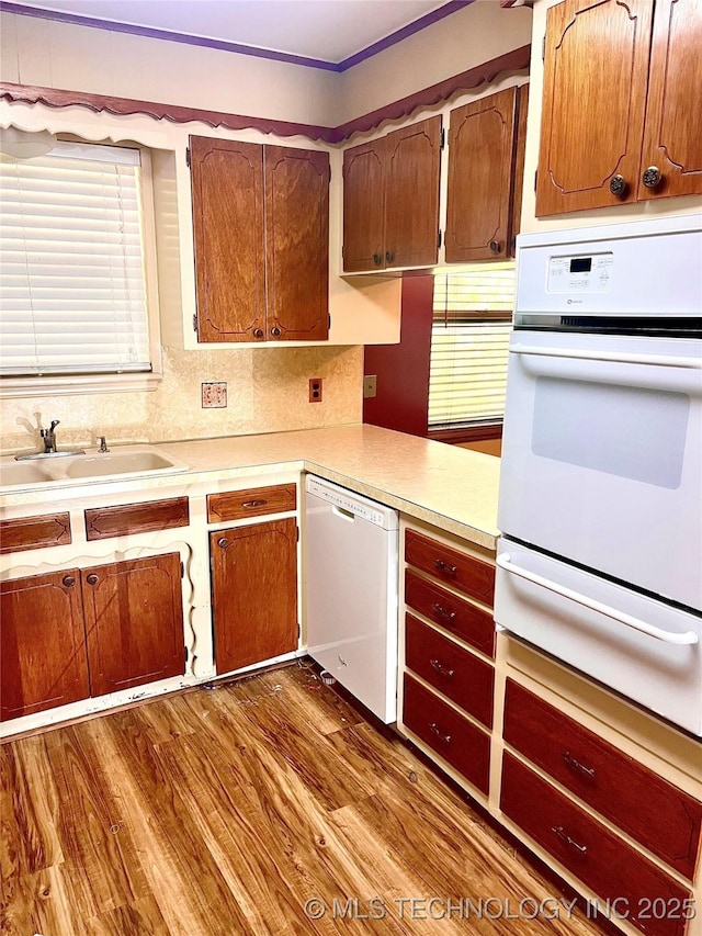 kitchen with a sink, brown cabinets, white appliances, a warming drawer, and light countertops