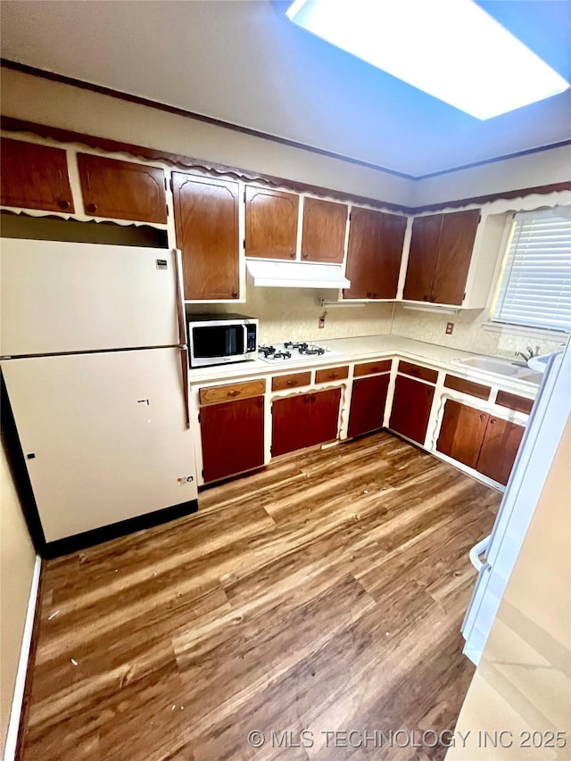 kitchen with a sink, light wood-style floors, white appliances, light countertops, and under cabinet range hood