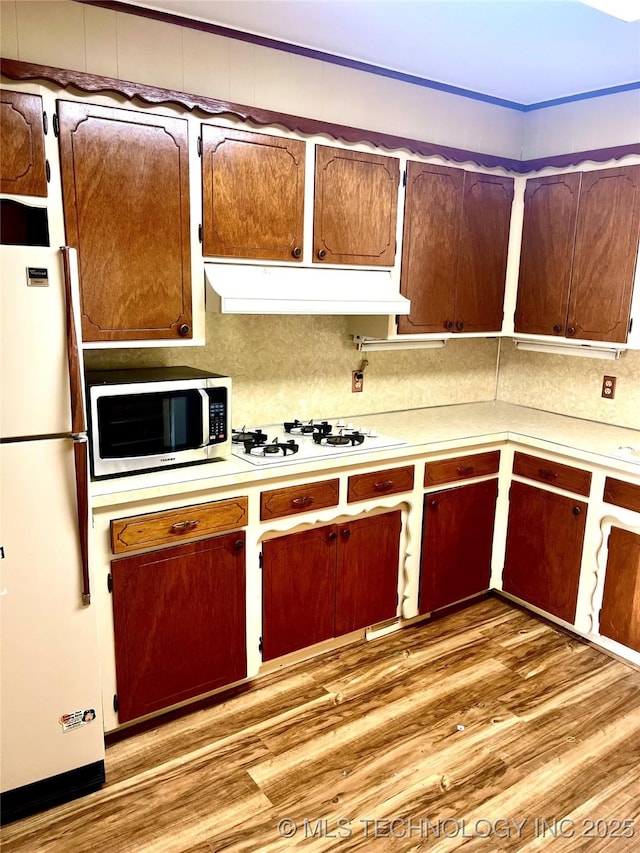kitchen with light wood finished floors, exhaust hood, light countertops, backsplash, and white appliances