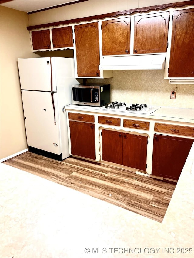 kitchen with ventilation hood, light wood-style floors, white appliances, brown cabinetry, and light countertops