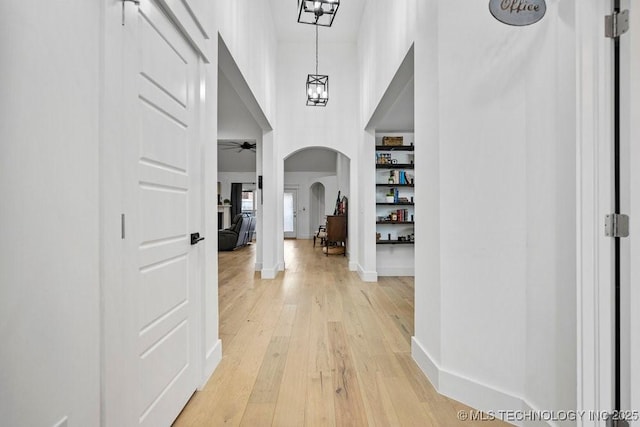 entryway featuring a ceiling fan, light wood-style floors, arched walkways, a towering ceiling, and baseboards