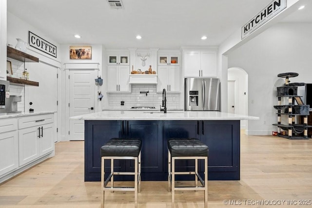 kitchen featuring tasteful backsplash, a center island with sink, light wood-style flooring, and stainless steel fridge with ice dispenser