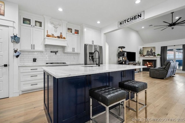 kitchen with a ceiling fan, white cabinets, light wood-style floors, stainless steel appliances, and backsplash