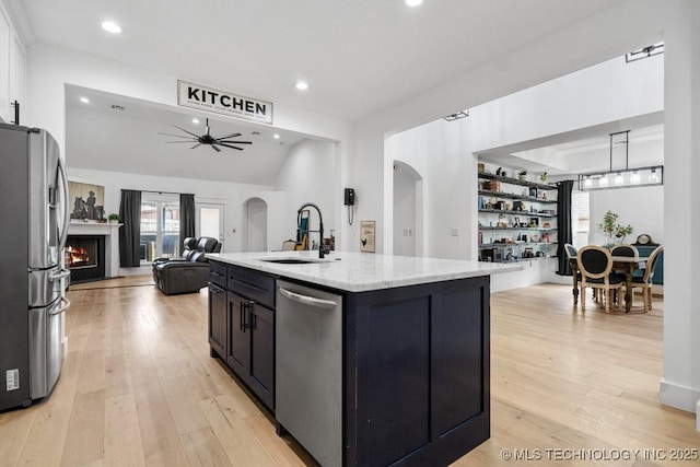 kitchen featuring stainless steel appliances, a warm lit fireplace, a sink, arched walkways, and open floor plan