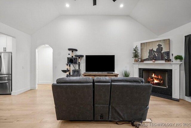 living room with arched walkways, light wood-type flooring, baseboards, a fireplace, and high vaulted ceiling