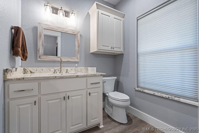 bathroom featuring toilet, baseboards, wood finished floors, a textured wall, and vanity