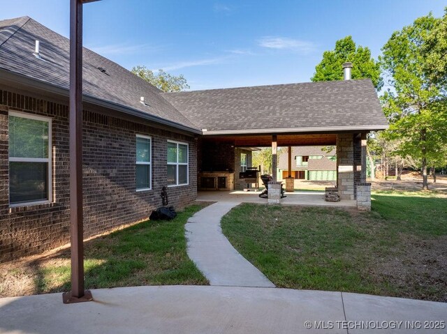 exterior space with a lawn, brick siding, a patio, and a shingled roof