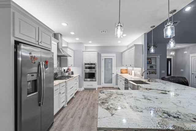 kitchen with wall chimney exhaust hood, stainless steel appliances, light wood-style flooring, a sink, and light stone counters