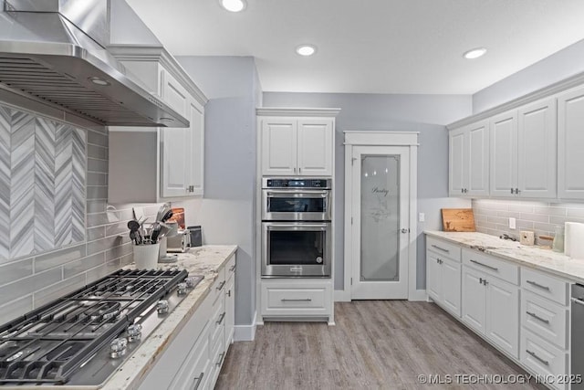kitchen featuring decorative backsplash, wall chimney exhaust hood, appliances with stainless steel finishes, and white cabinetry