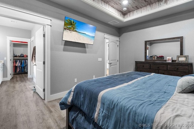 bedroom featuring a tray ceiling, visible vents, light wood finished floors, and baseboards