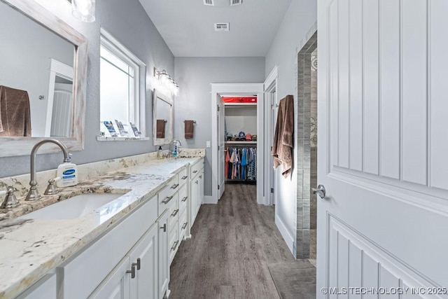 full bathroom featuring wood finished floors, a sink, a spacious closet, double vanity, and visible vents