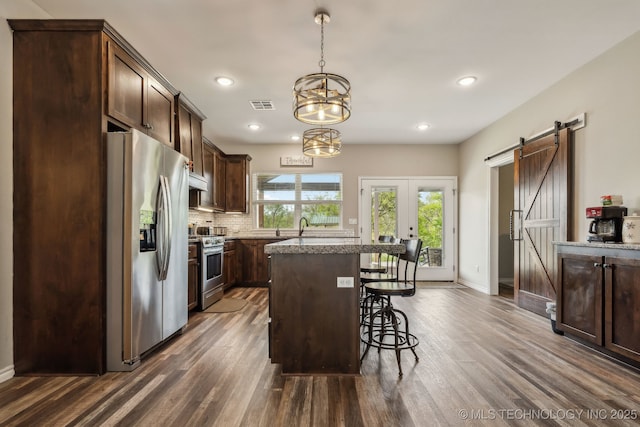 kitchen featuring dark brown cabinetry, appliances with stainless steel finishes, a breakfast bar area, visible vents, and dark wood-style floors
