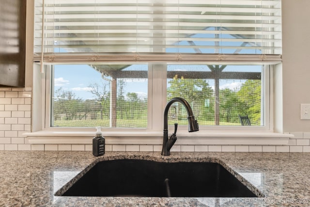 interior details with a sink, decorative backsplash, and stone counters