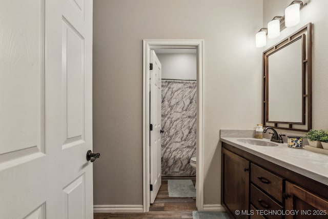 bathroom featuring toilet, baseboards, wood finished floors, and vanity