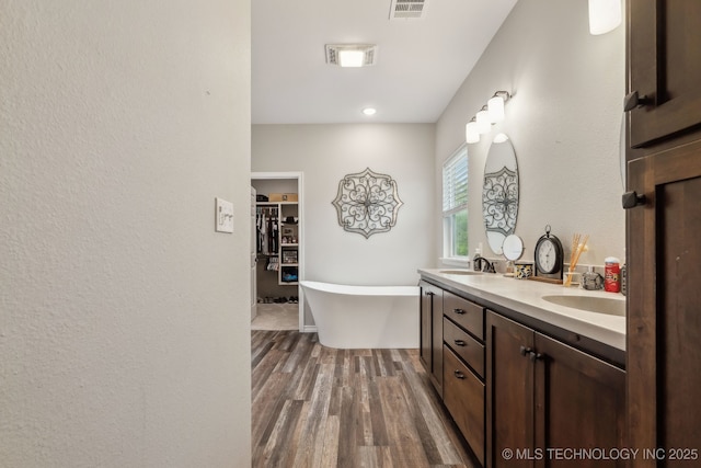 full bathroom featuring double vanity, visible vents, wood finished floors, a sink, and a soaking tub