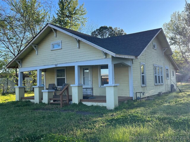 bungalow featuring a shingled roof, covered porch, and a front yard