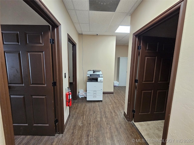 corridor with baseboards, wood finished floors, and a drop ceiling