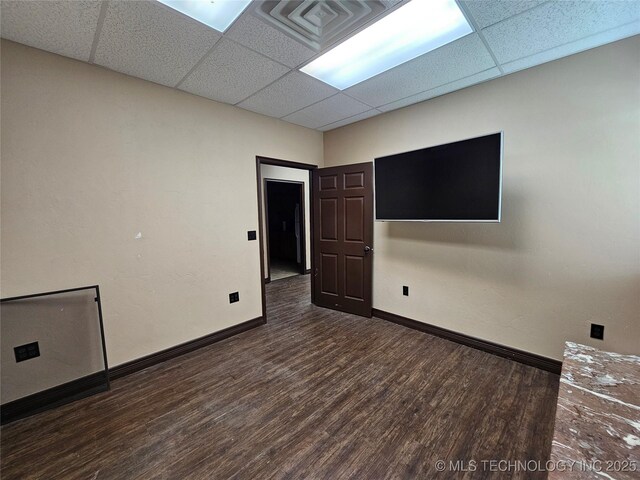 empty room with dark wood-type flooring, a paneled ceiling, visible vents, and baseboards