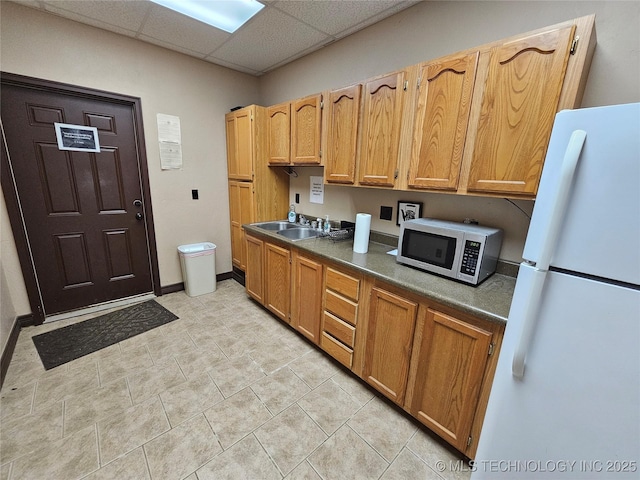 kitchen featuring dark countertops, a paneled ceiling, freestanding refrigerator, and a sink