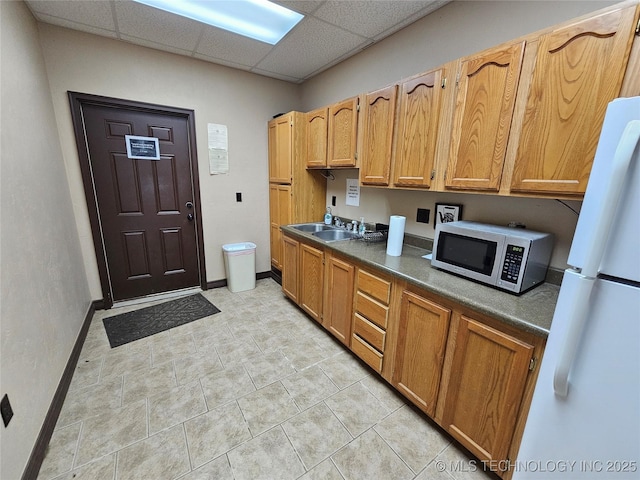 kitchen with dark countertops, a sink, stainless steel microwave, a paneled ceiling, and freestanding refrigerator