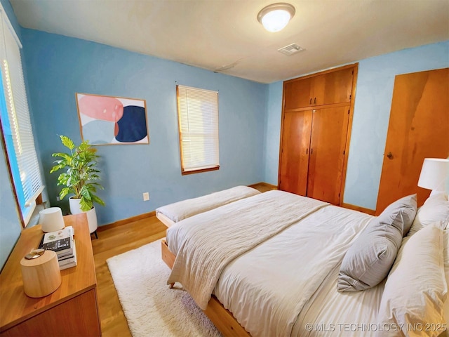 bedroom featuring baseboards, wood finished floors, visible vents, and a closet