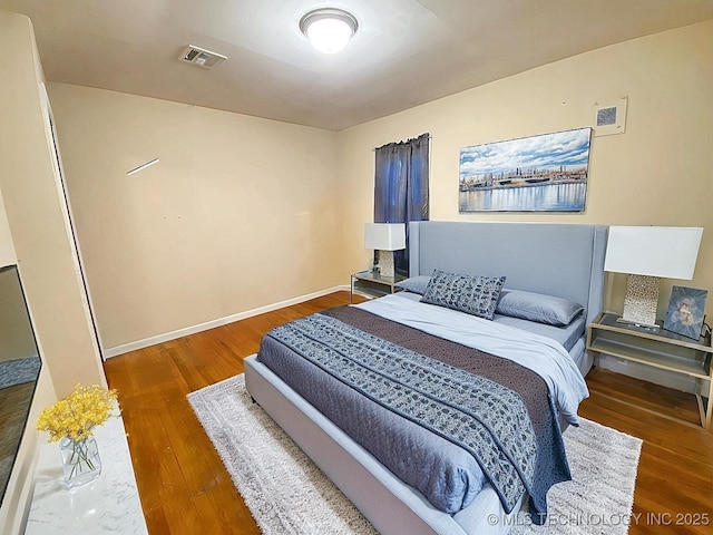 bedroom with wood finished floors, visible vents, and baseboards