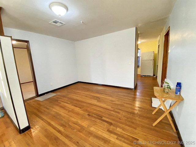 unfurnished room featuring wood-type flooring, visible vents, and baseboards