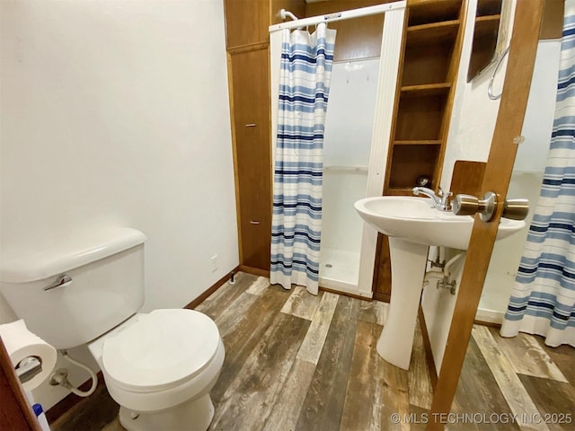 full bathroom featuring baseboards, wood finished floors, toilet, and a stall shower