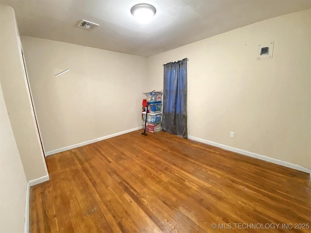 empty room featuring hardwood / wood-style floors, visible vents, and baseboards