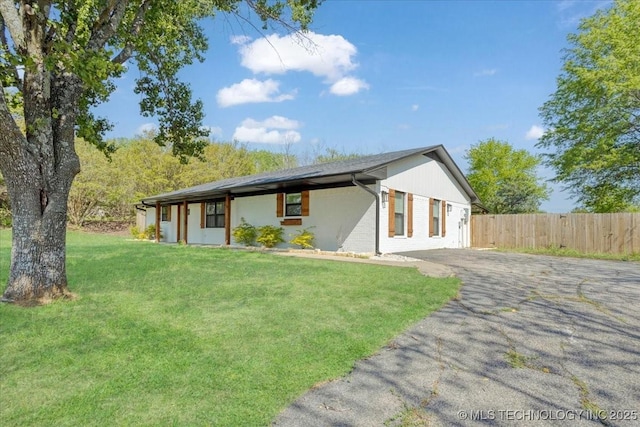 exterior space featuring brick siding, driveway, fence, and a lawn