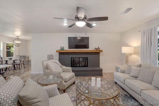 living area featuring wood finished floors, ceiling fan with notable chandelier, a glass covered fireplace, baseboards, and visible vents