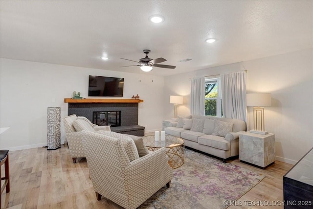 living room featuring light wood-style floors, a glass covered fireplace, baseboards, and ceiling fan