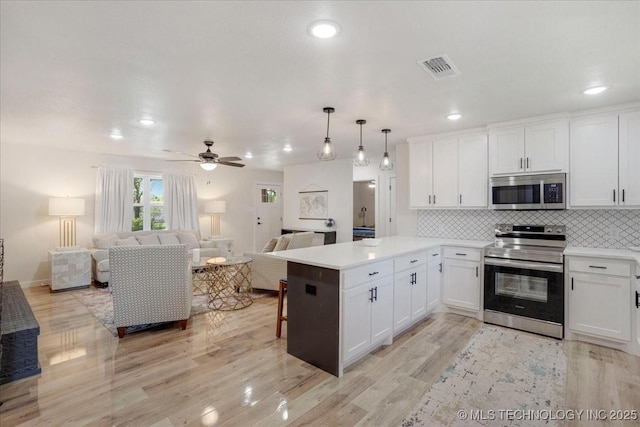 kitchen featuring a peninsula, open floor plan, white cabinetry, and appliances with stainless steel finishes