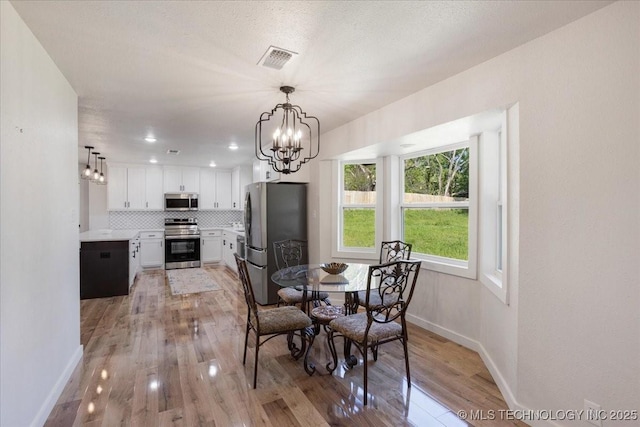 dining room with baseboards, a notable chandelier, visible vents, and light wood-type flooring